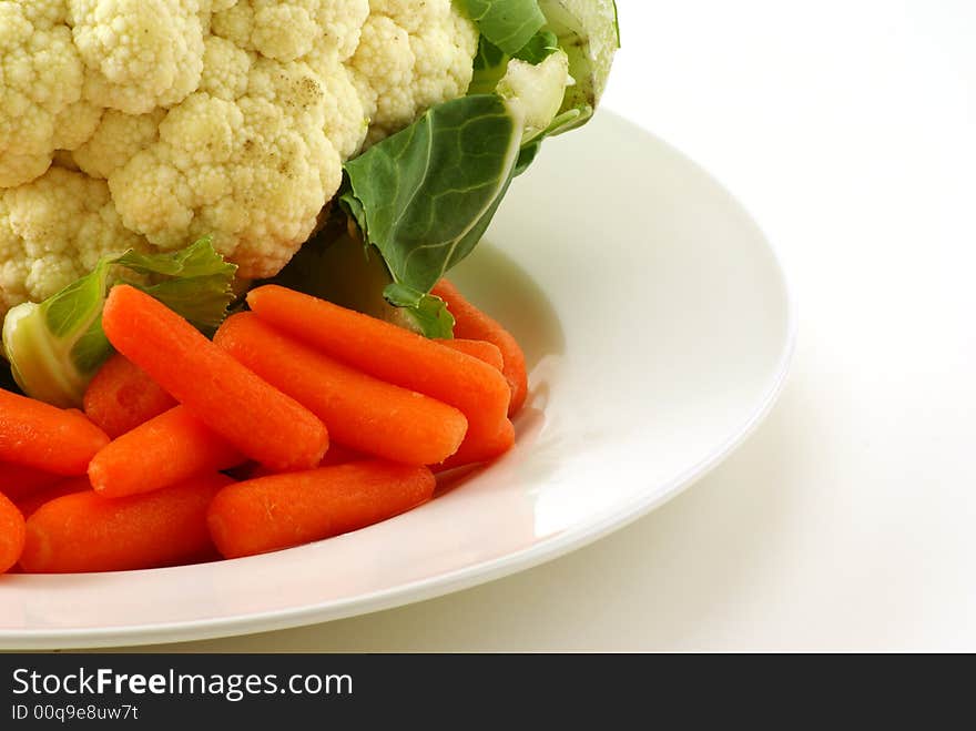 Raw cauliflower and baby carrots on white plate with greenery. Raw cauliflower and baby carrots on white plate with greenery.