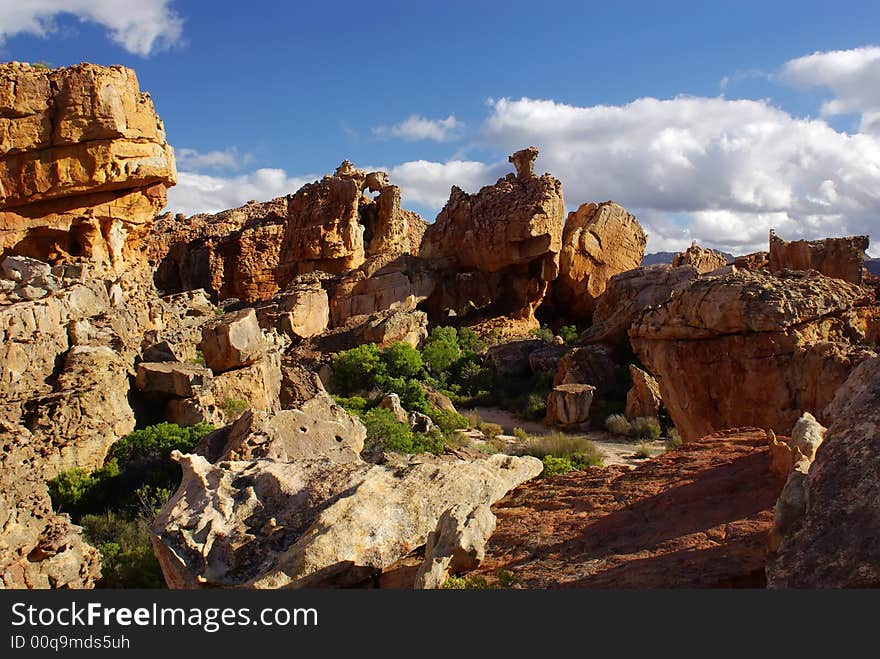 Yellow red stones and cliffs on red soil. Yellow sand and green bushes, deep blue cloudy sky. mountains of South Africa. Yellow red stones and cliffs on red soil. Yellow sand and green bushes, deep blue cloudy sky. mountains of South Africa