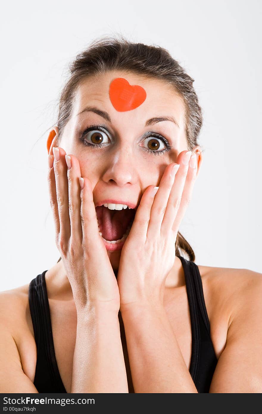 Attractive woman with red heartshaped plaster on forehead. Seems to be totally surprised. Attractive woman with red heartshaped plaster on forehead. Seems to be totally surprised