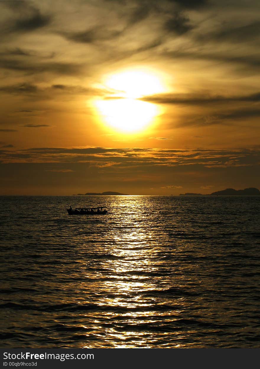 A setting sun by the sea with a boat cruising through its reflection. A setting sun by the sea with a boat cruising through its reflection