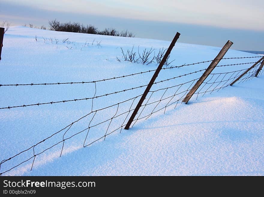 Barbed wire fence in winter, partly covered in snow. Barbed wire fence in winter, partly covered in snow