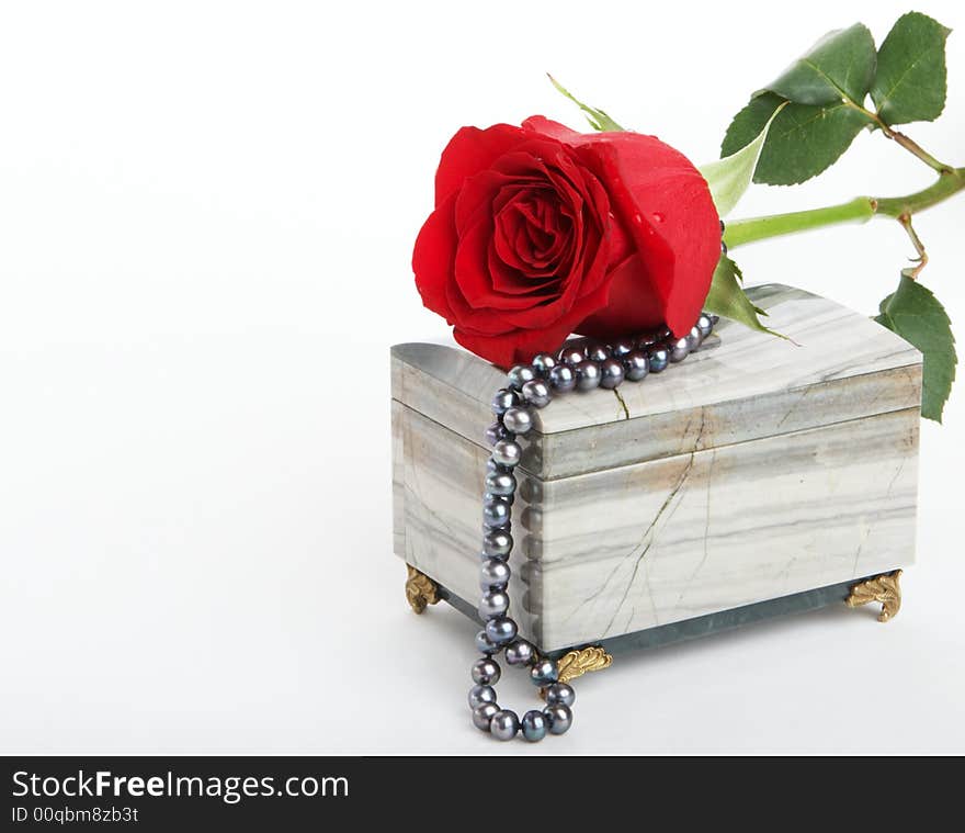 Beautiful red rose lying on box with black pearls