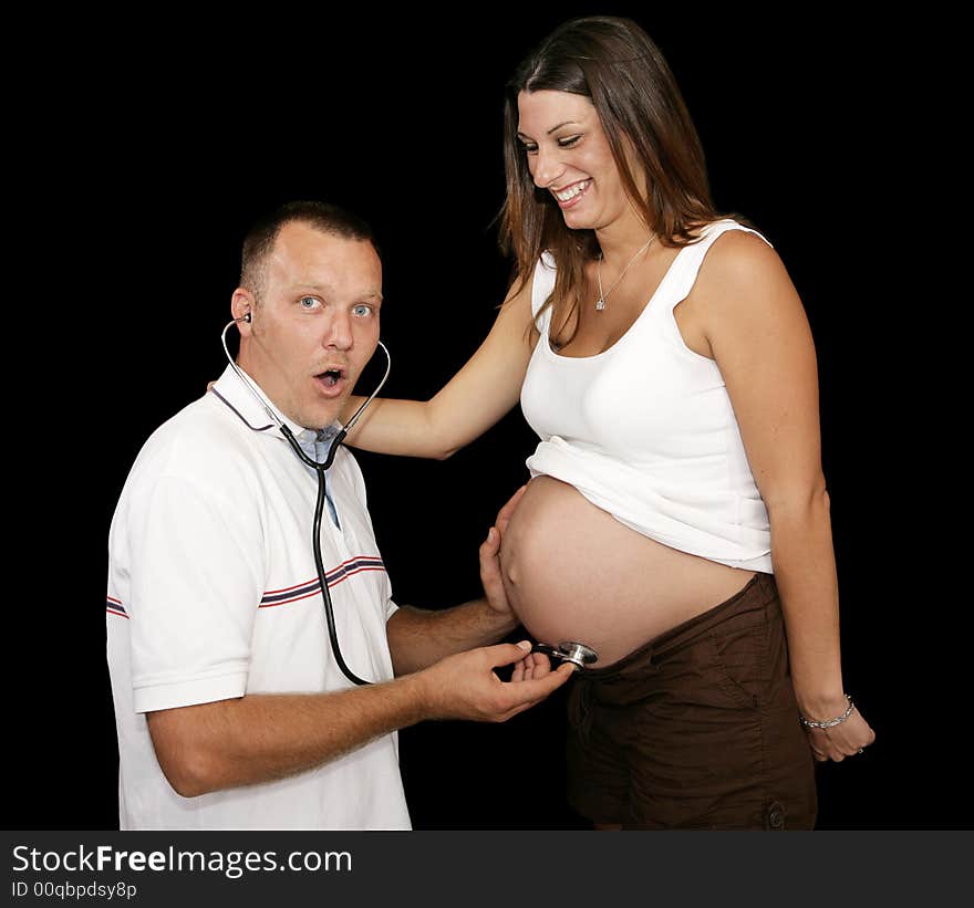 New father listening to his wife's pregnant belly with a stethescope.  Black background. New father listening to his wife's pregnant belly with a stethescope.  Black background