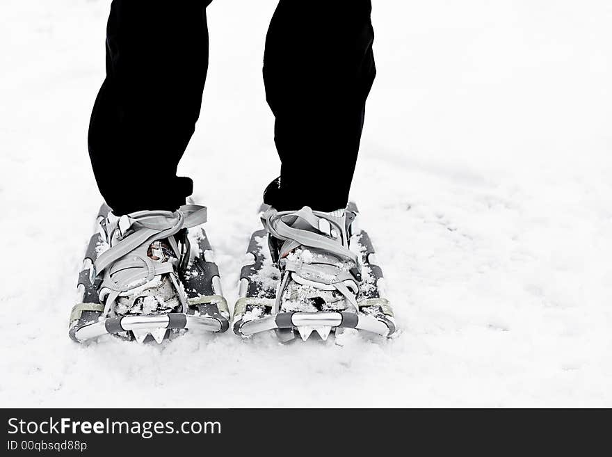 Someone wearing snowshoes in the snow.  Bottom half of legs down.