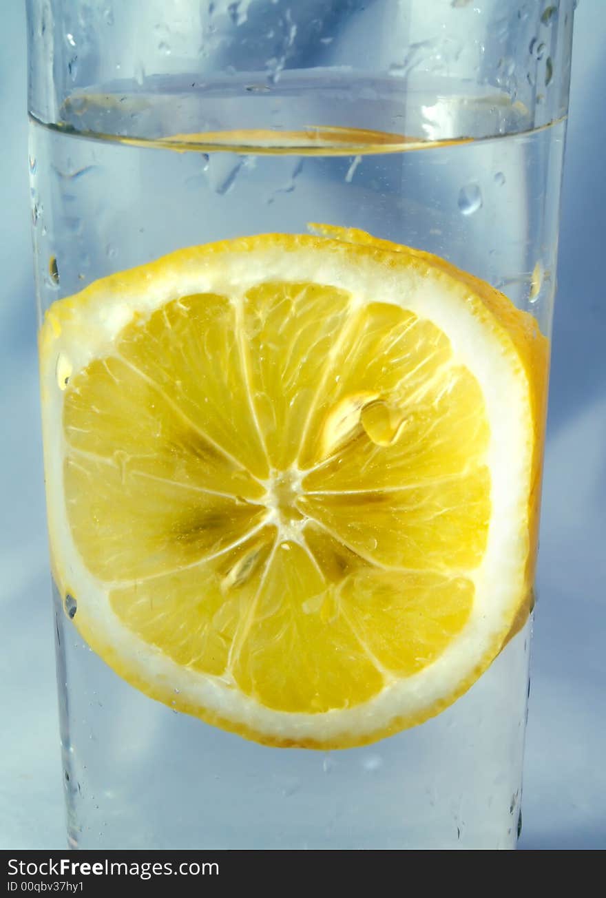 A fresh slice of lemon in a glass, on a blue background