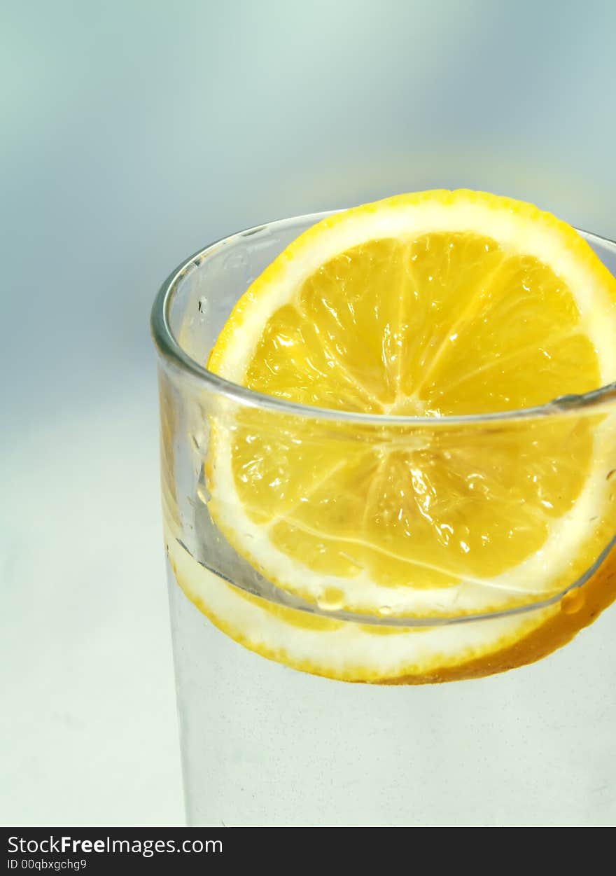 A fresh slice of lemon in a glass, on a blue background