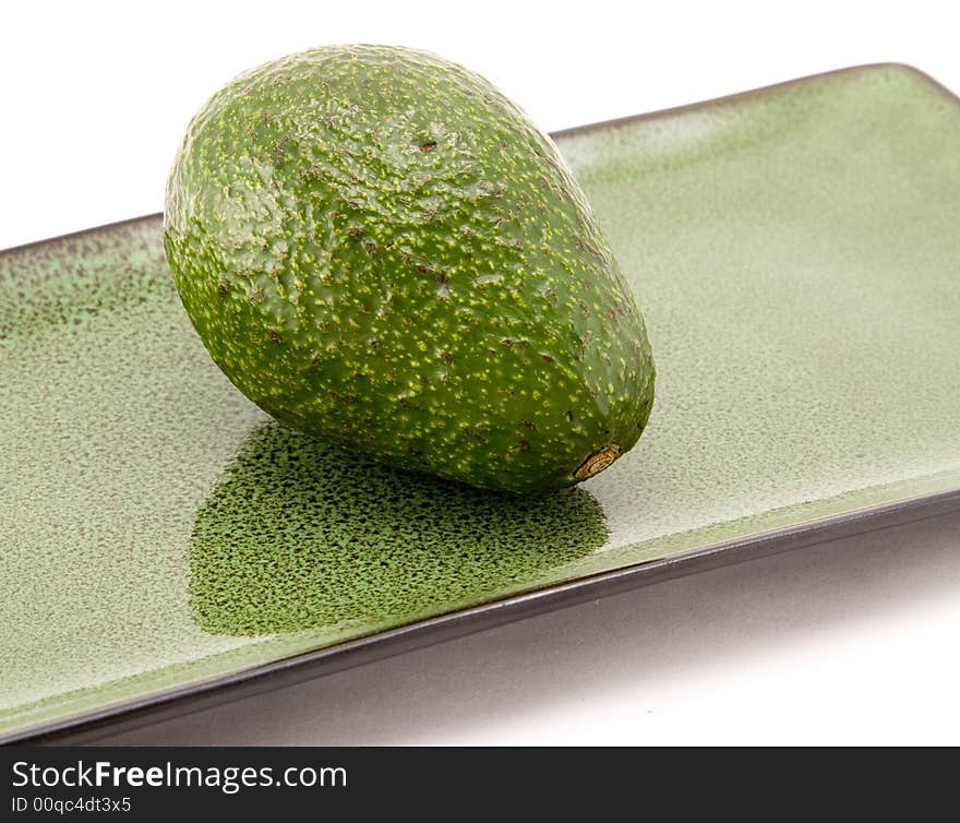 Whole avocado on avacado colored plate isolated on white background. Whole avocado on avacado colored plate isolated on white background.