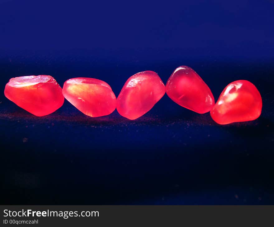 Five red grains of a pomegranate on a dark background