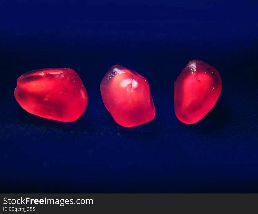 Three red grains of a pomegranate on a dark background