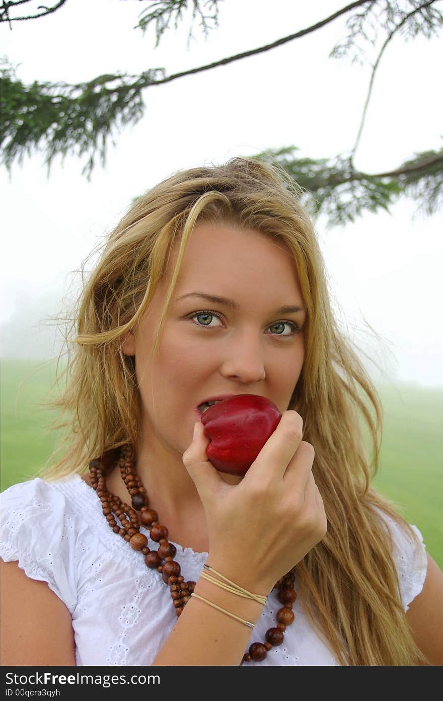 A pretty young blonde girl takes her first bite of a crisp red apple