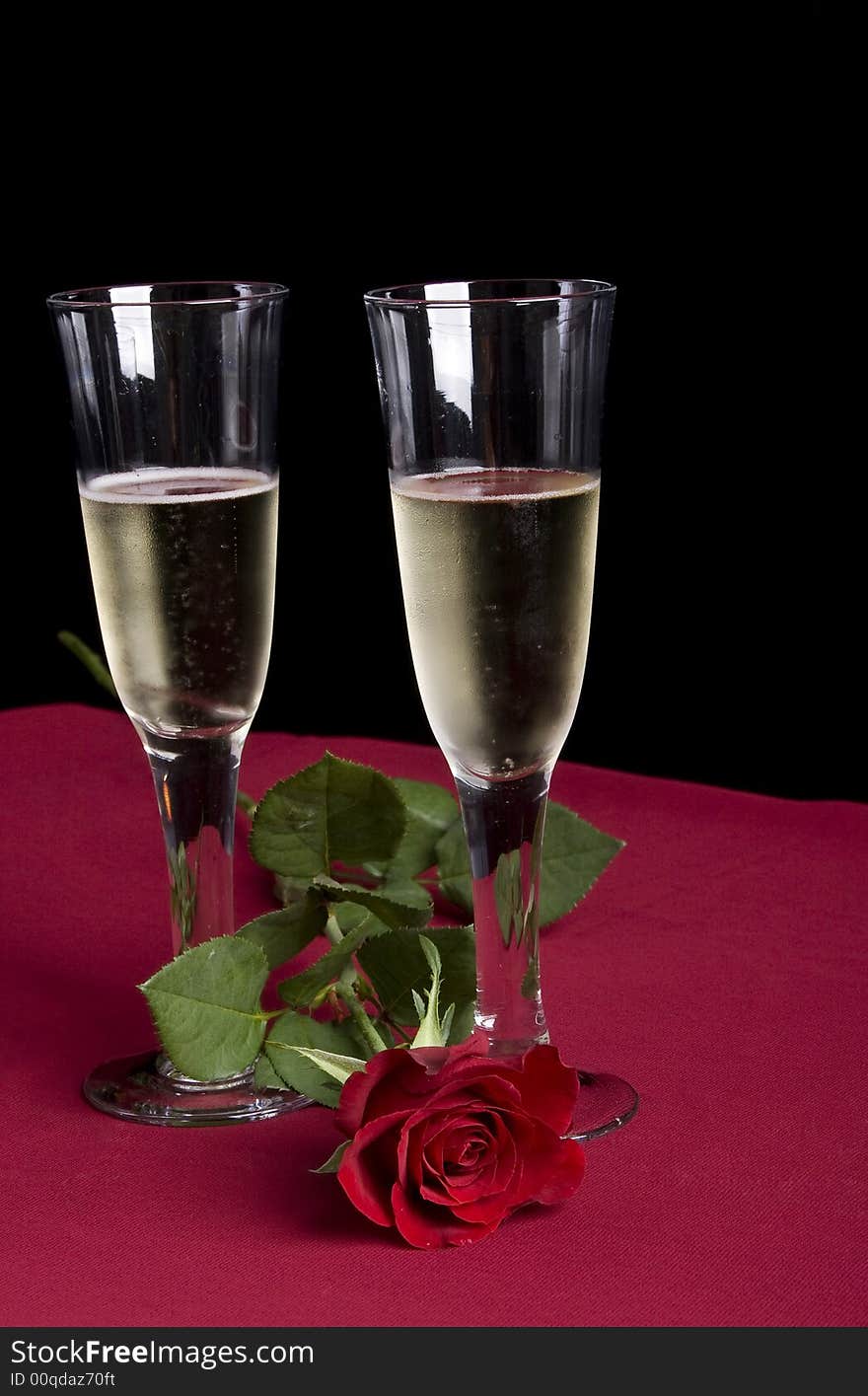 Two glassis of champagne with a single red rose on a red and black background. Two glassis of champagne with a single red rose on a red and black background