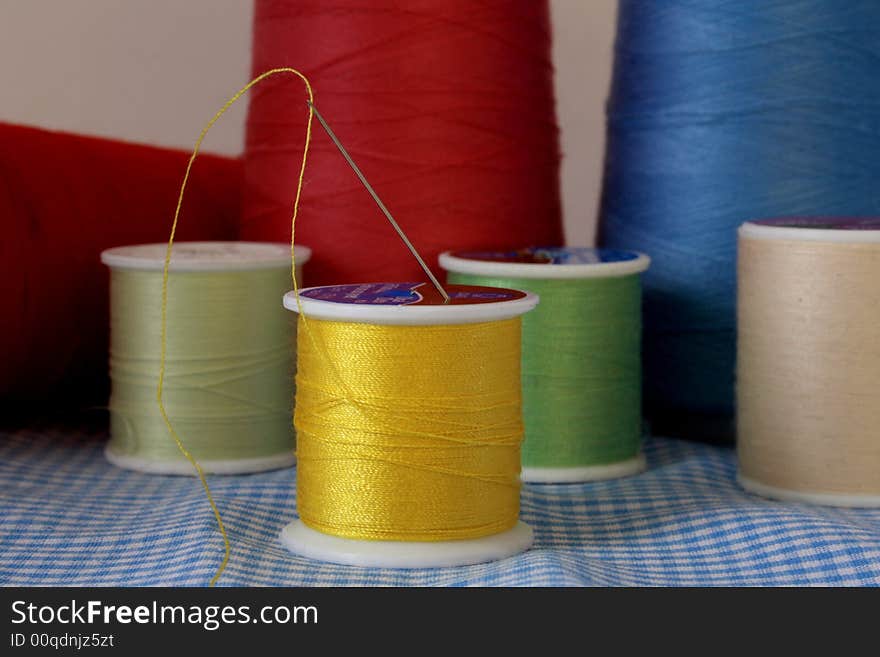 Yellow spool of thread with needle on a white background with other colored spools of thread