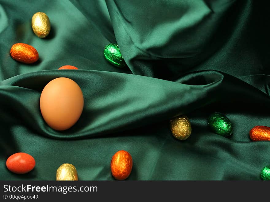 A selection of Easter eggs (natural and chocolate) lying on dark green satin fabric. A selection of Easter eggs (natural and chocolate) lying on dark green satin fabric.