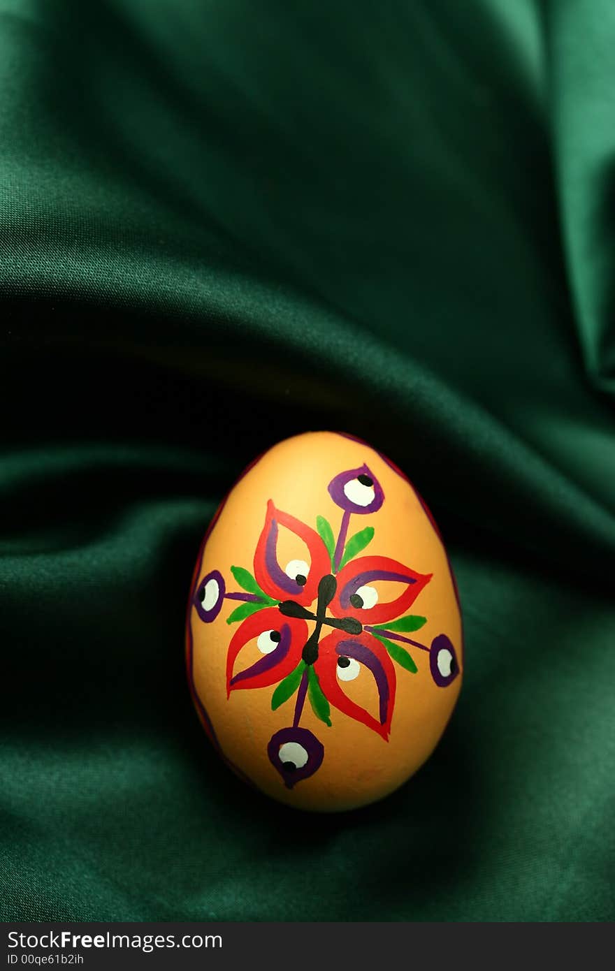 A detail of an Easter egg with colorful ornaments, lying on dark green satin fabric - background. A detail of an Easter egg with colorful ornaments, lying on dark green satin fabric - background.