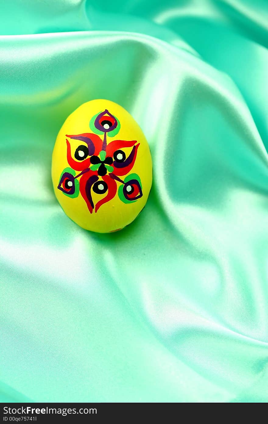 A detail of a yellow handpainted Easter egg on turquoise satin fabric - background.