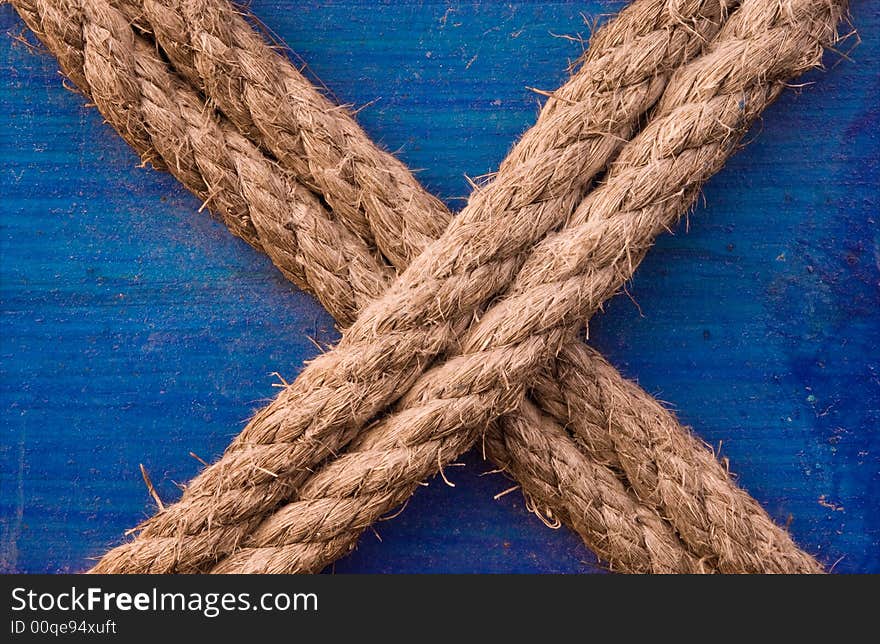 Image shows a double rope in an X letter formation, tied to a blue painted wooden surface. Image shows a double rope in an X letter formation, tied to a blue painted wooden surface