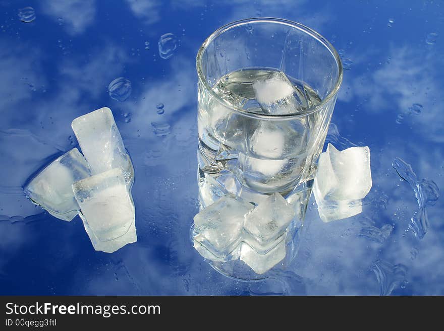 Glass of water with ice on background with blue sky and clouds. Glass of water with ice on background with blue sky and clouds