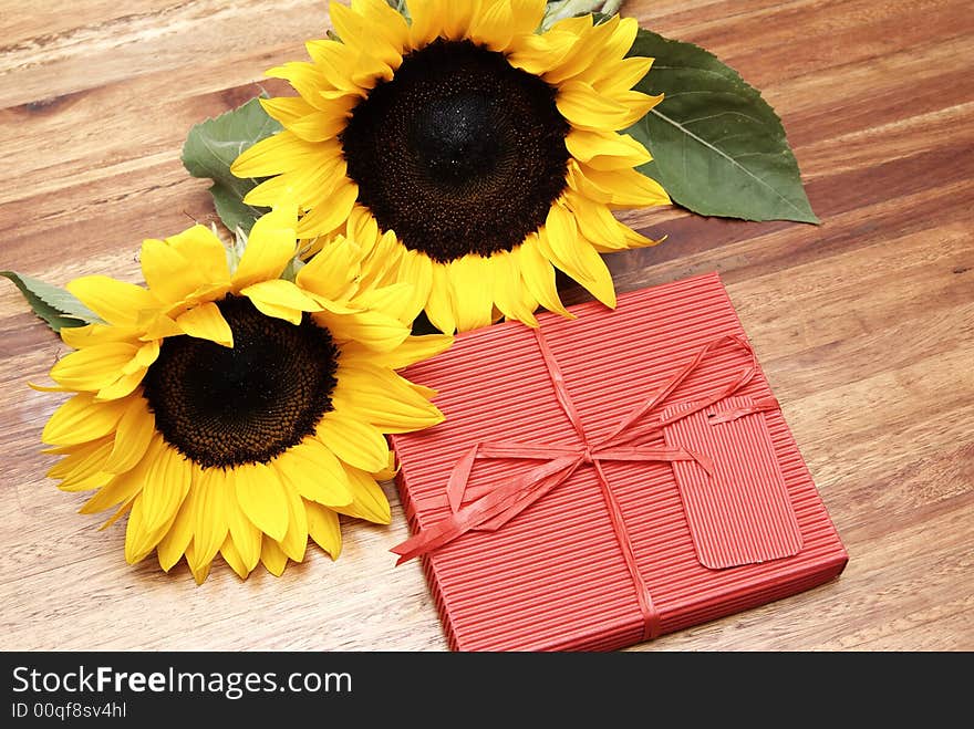 Two sunflowers and a red box on a wooden table