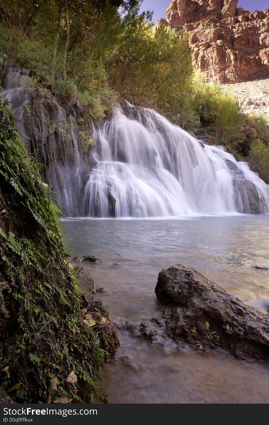 Navaho Falls cascading into aqua pool with green foliage and red rock cliff as background Havasupai Indian Reservation