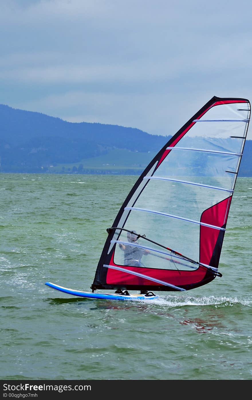 A board sailor speeds across a mountain lake. Space for text on the sky. A board sailor speeds across a mountain lake. Space for text on the sky.