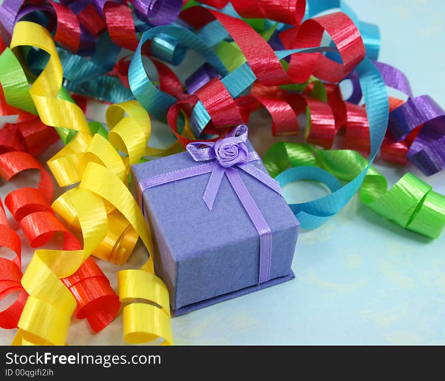 A small light purple gift box is nestled in a pile of colorful curly ribbon. A small light purple gift box is nestled in a pile of colorful curly ribbon.