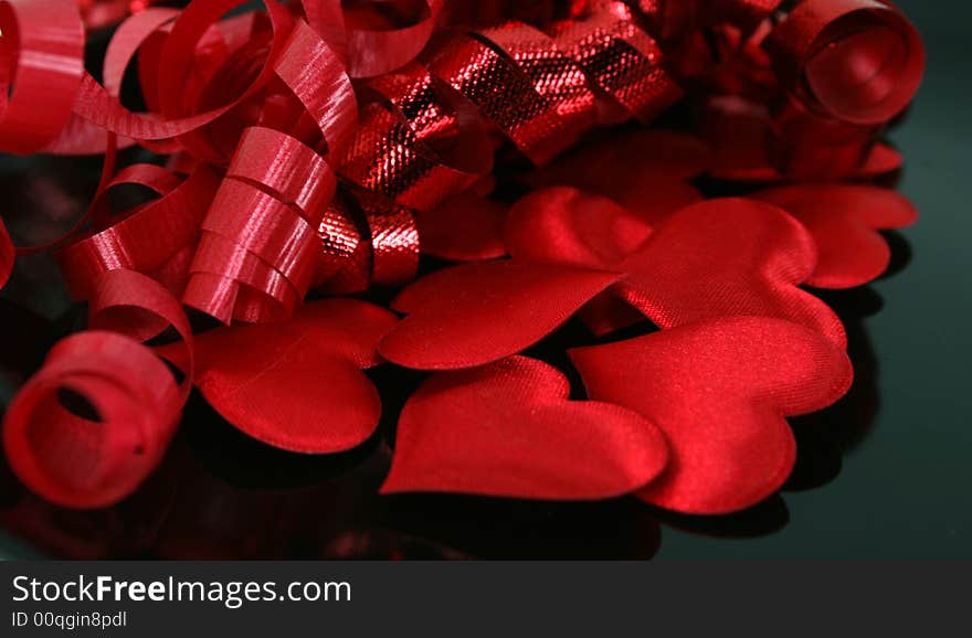 Puffy, red satin hearts with curly red ribbon on a reflective black surface. Puffy, red satin hearts with curly red ribbon on a reflective black surface.