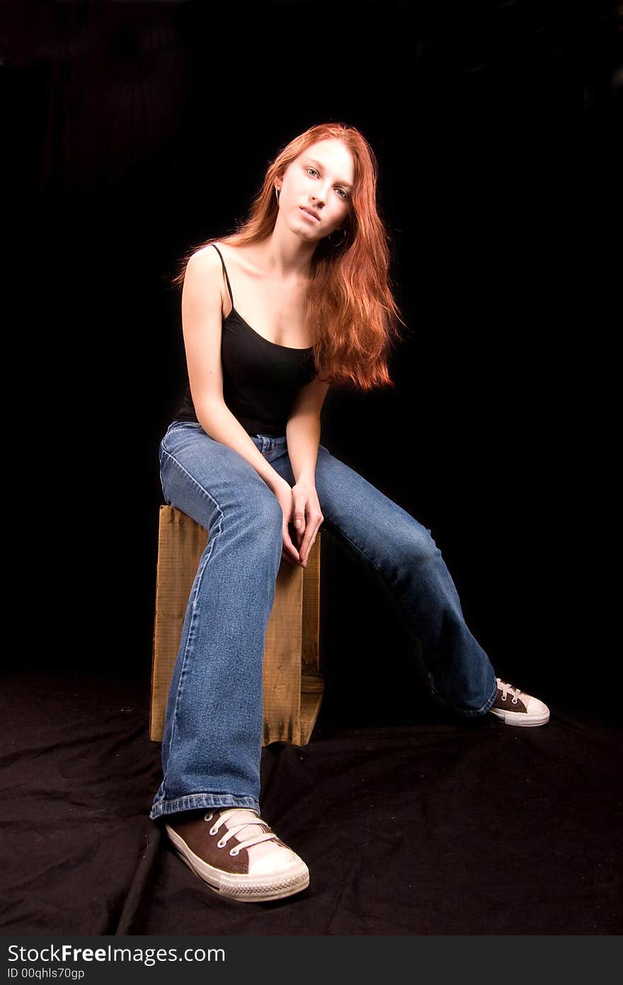 Beautiful thin redhead seated on wooden crate. Beautiful thin redhead seated on wooden crate