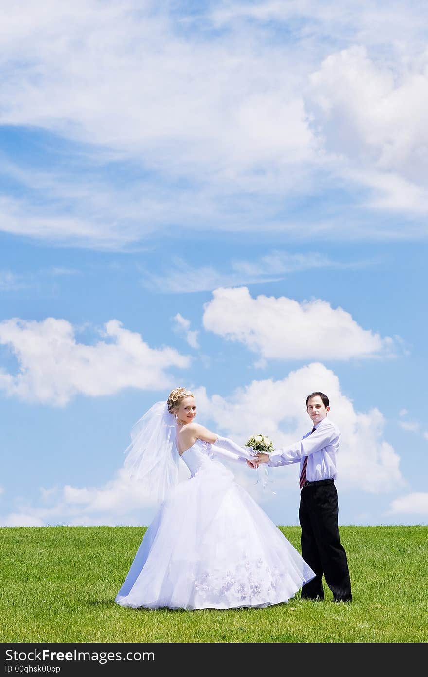 Newly-married couple on a green grass under the blue sky