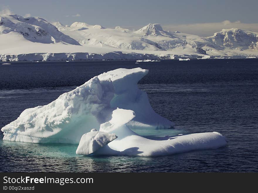 Single iceberg in Lemaire Channel with glacier covered mountains and blue sky as background Antarctica