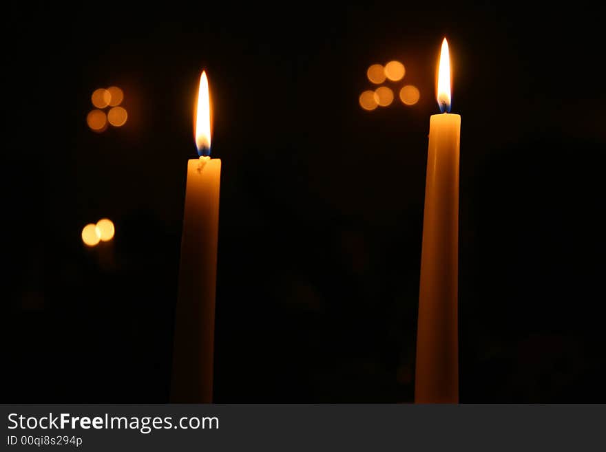 Two Candles burning at night with other lights out of focus in the background