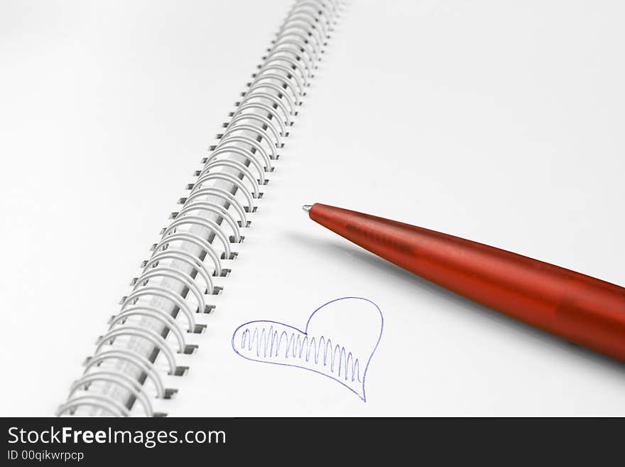 Open spiral notebook with red plastic pen and blue heart. Open spiral notebook with red plastic pen and blue heart.