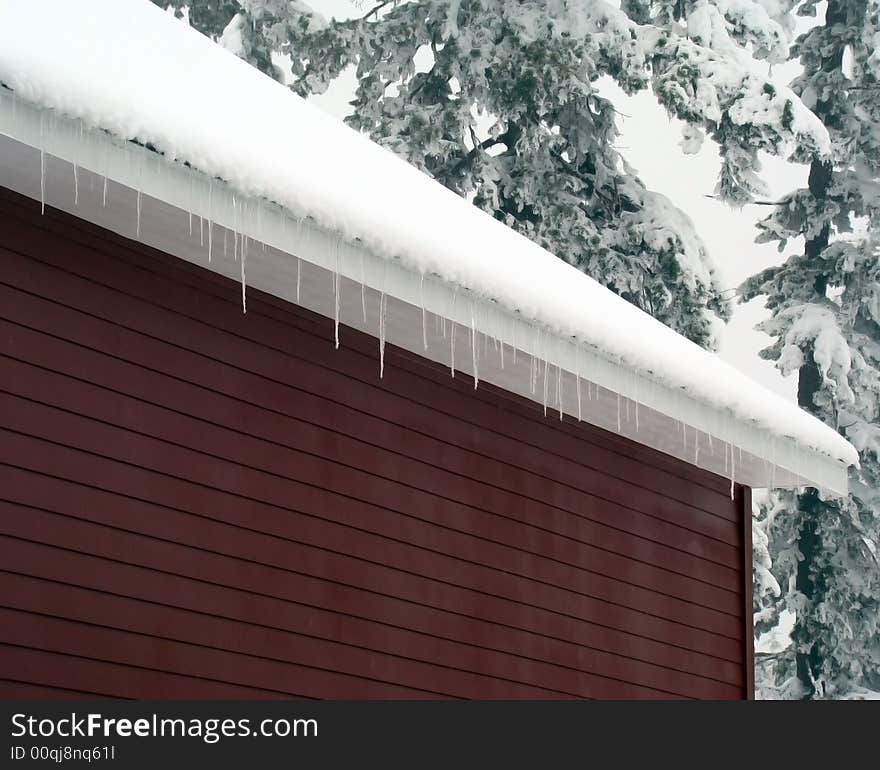 A picture of the eaves of a garage in winter with ice crystals hanging of the edge.