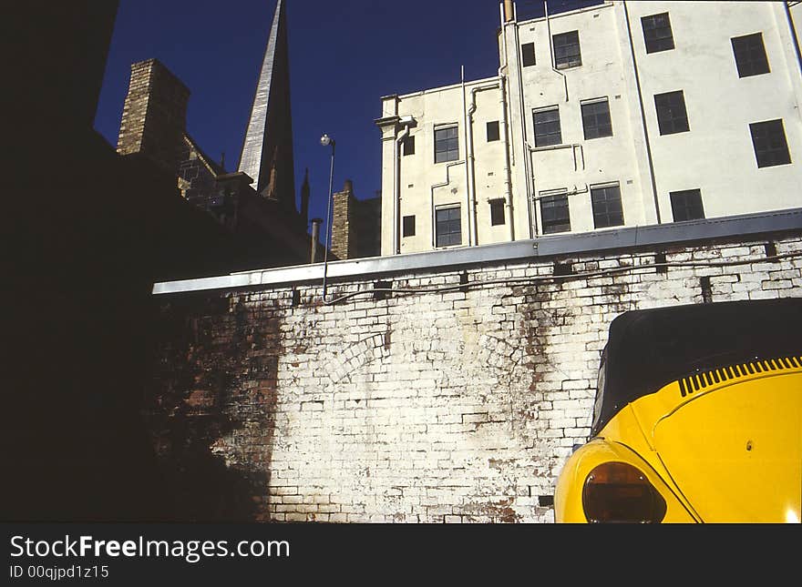 An VW Beetle parked against an old brick wall contrasts with the city skyline. An VW Beetle parked against an old brick wall contrasts with the city skyline