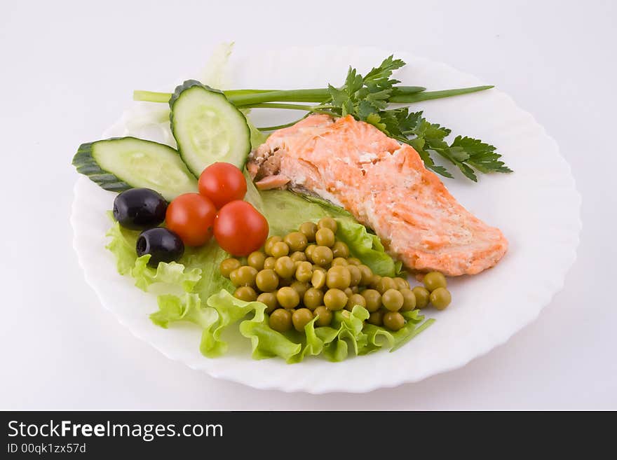 Stake from a trout with vegetables and green peas on a plate on a white background