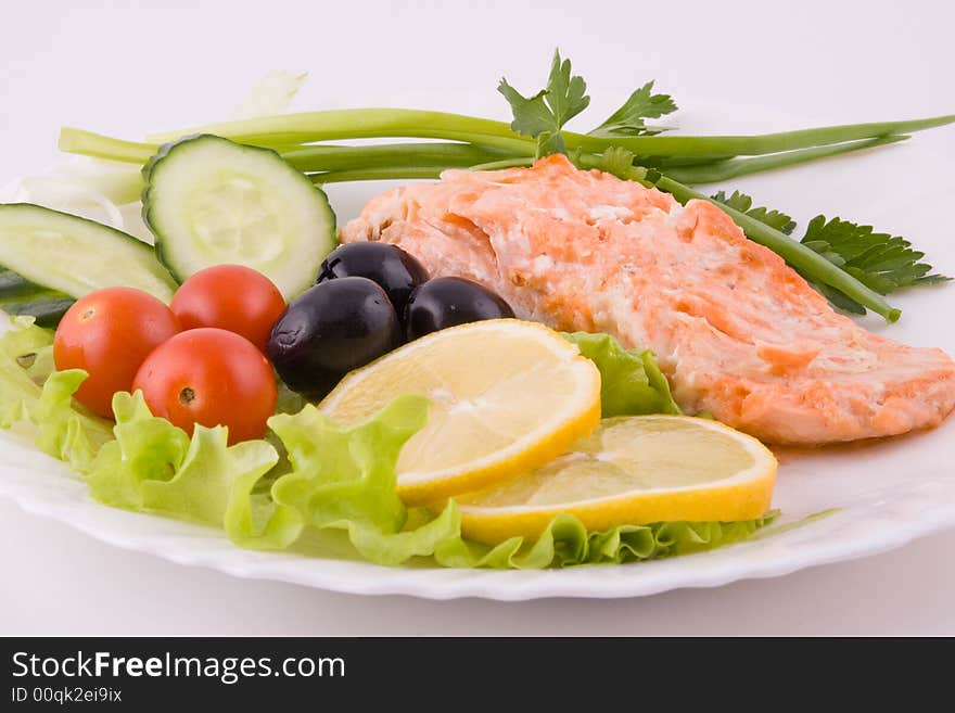 Stake from a trout with vegetables and a lemon on a plate on a white background