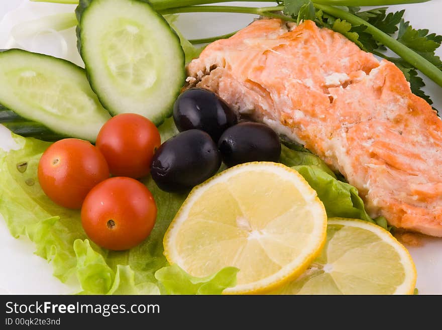 Stake from a trout with vegetables and a lemon on a plate on a white background