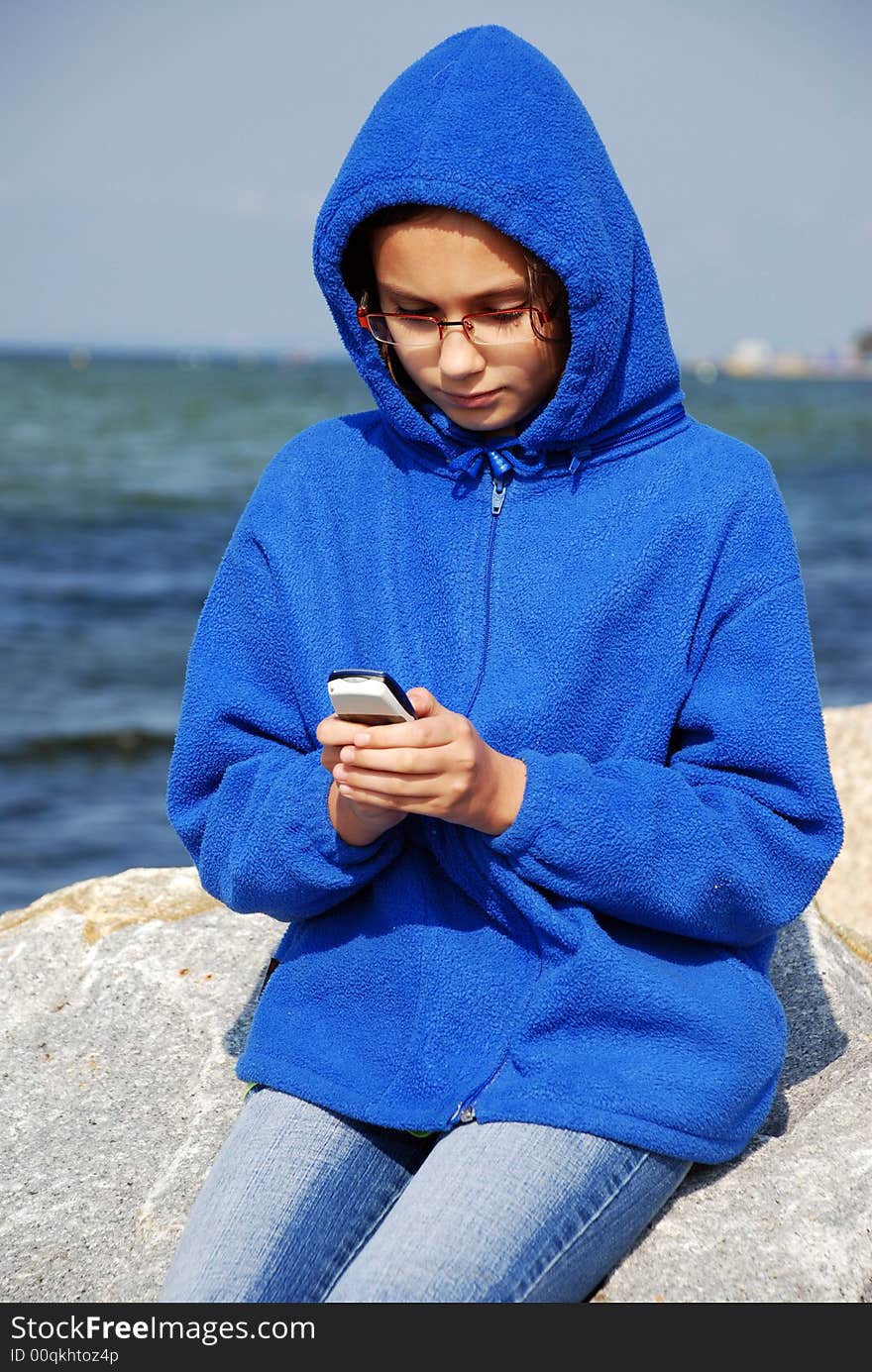 Young girl sitting on a rocks with mobile phnone at the seaside on cold and windy day. Young girl sitting on a rocks with mobile phnone at the seaside on cold and windy day.