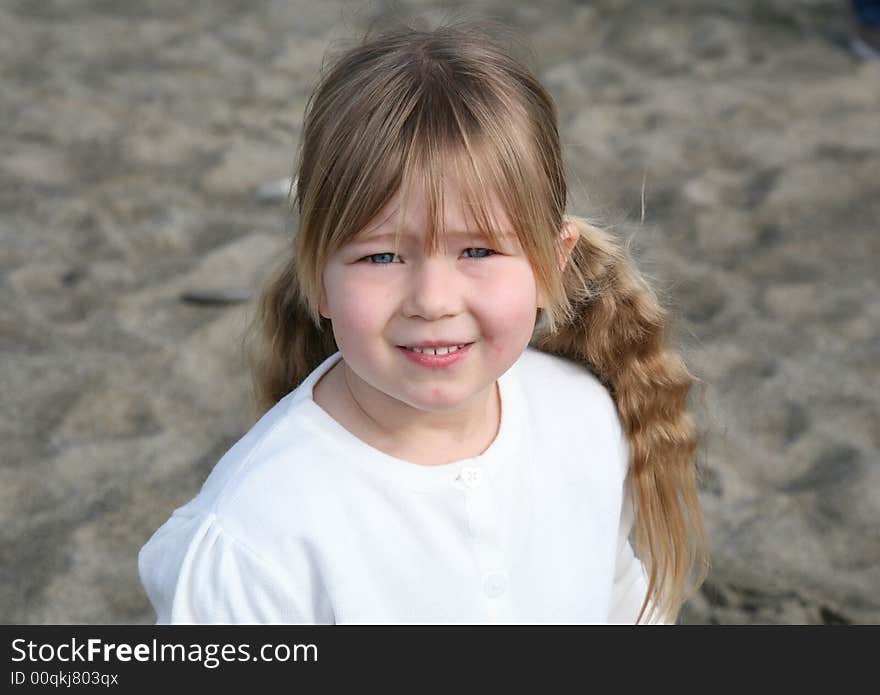 A young girl stood on the beach wearing a white jumper, looking at the camera. A young girl stood on the beach wearing a white jumper, looking at the camera