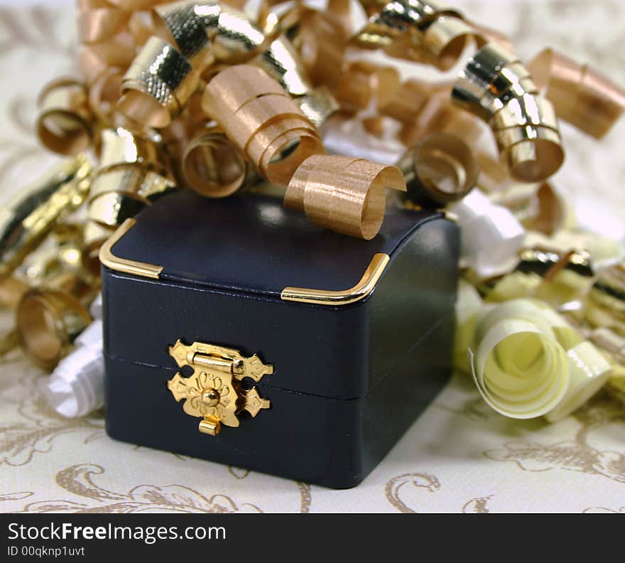 A small closed navy blue jewelry box surrounded by curly gold, white and yellow ribbon. A small closed navy blue jewelry box surrounded by curly gold, white and yellow ribbon.