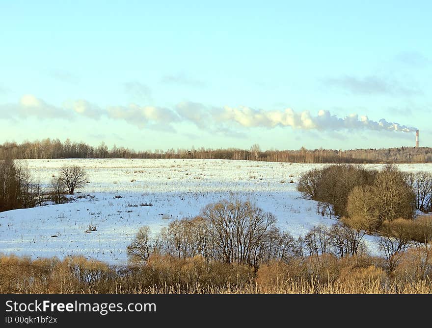 Winter landscape, the Long smoke loop from the pipe of industrial enterprise stretches above the forest, light, blue, cold sky. Winter landscape, the Long smoke loop from the pipe of industrial enterprise stretches above the forest, light, blue, cold sky.