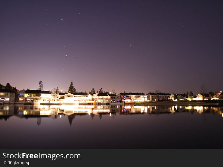 Lake side houses at night with great sky and light reflection.