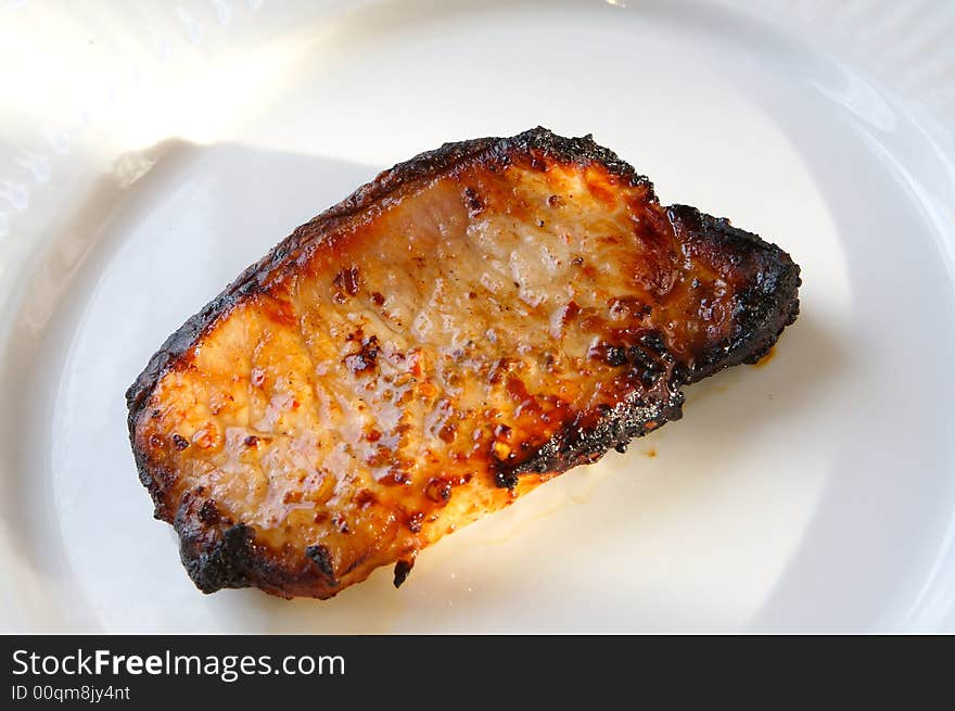 Pork loin chop grilled in th summer sunlight on a white plate. Pork loin chop grilled in th summer sunlight on a white plate