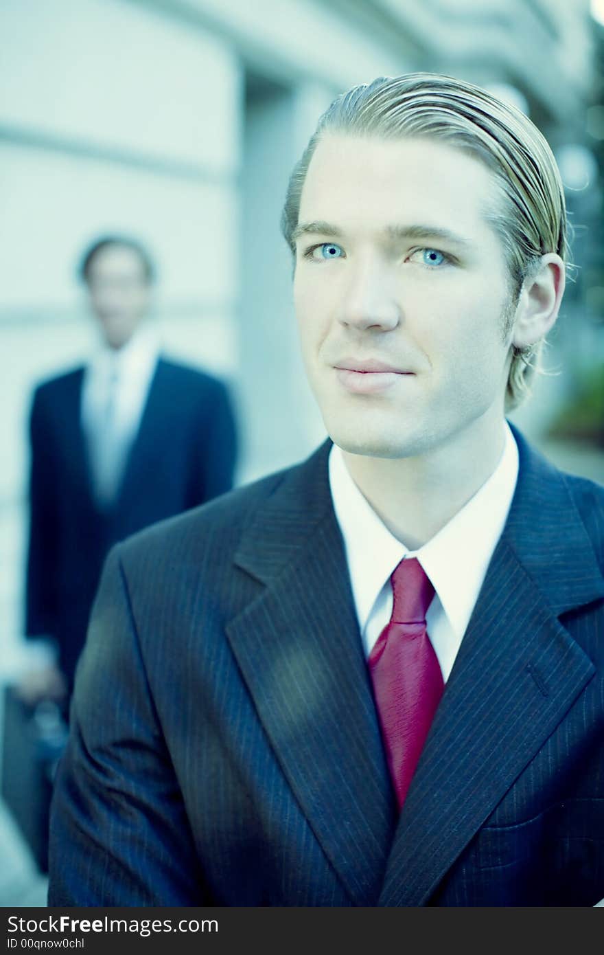 Two businessmen standing looking at camera in full suit in front of building