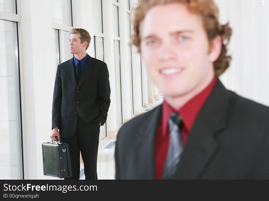 Two businessmen in an office hallway, once pauses to smile.