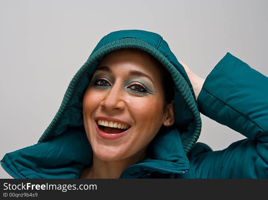 Beautiful smiling young woman wearing a green winter coat with the hood over her head and her hand behind her head, isolated on white. Beautiful smiling young woman wearing a green winter coat with the hood over her head and her hand behind her head, isolated on white