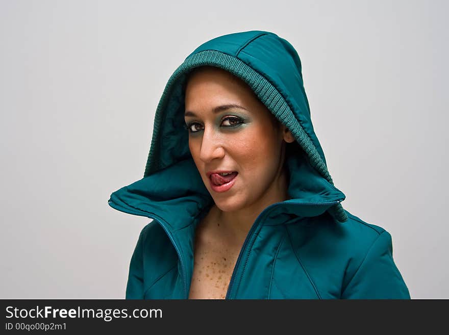 A young woman licking her lips, wearing a green winter coat zipped open and the hood covering her head, isolated on white. A young woman licking her lips, wearing a green winter coat zipped open and the hood covering her head, isolated on white