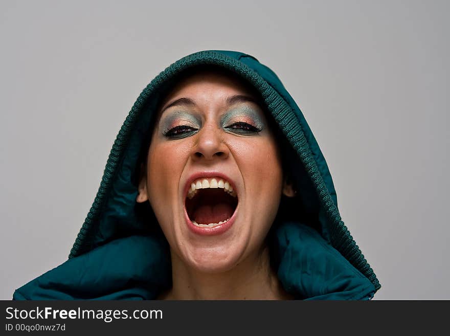 A beautiful young woman screaming aggressively wearing a green winter coat and the hood over her head, isolated on white. A beautiful young woman screaming aggressively wearing a green winter coat and the hood over her head, isolated on white