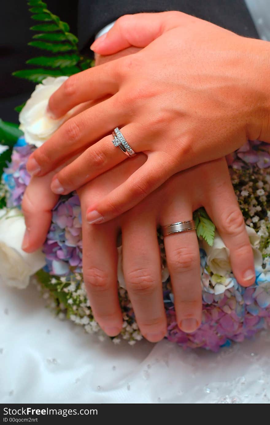 A bride and groom's hands and rings over the bride's bouquet. A bride and groom's hands and rings over the bride's bouquet.