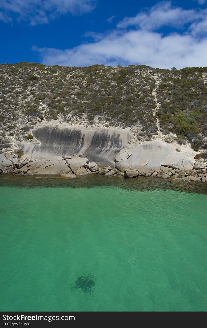 View on rocky seashore with a stingray swimming in green/turquoise water. View on rocky seashore with a stingray swimming in green/turquoise water