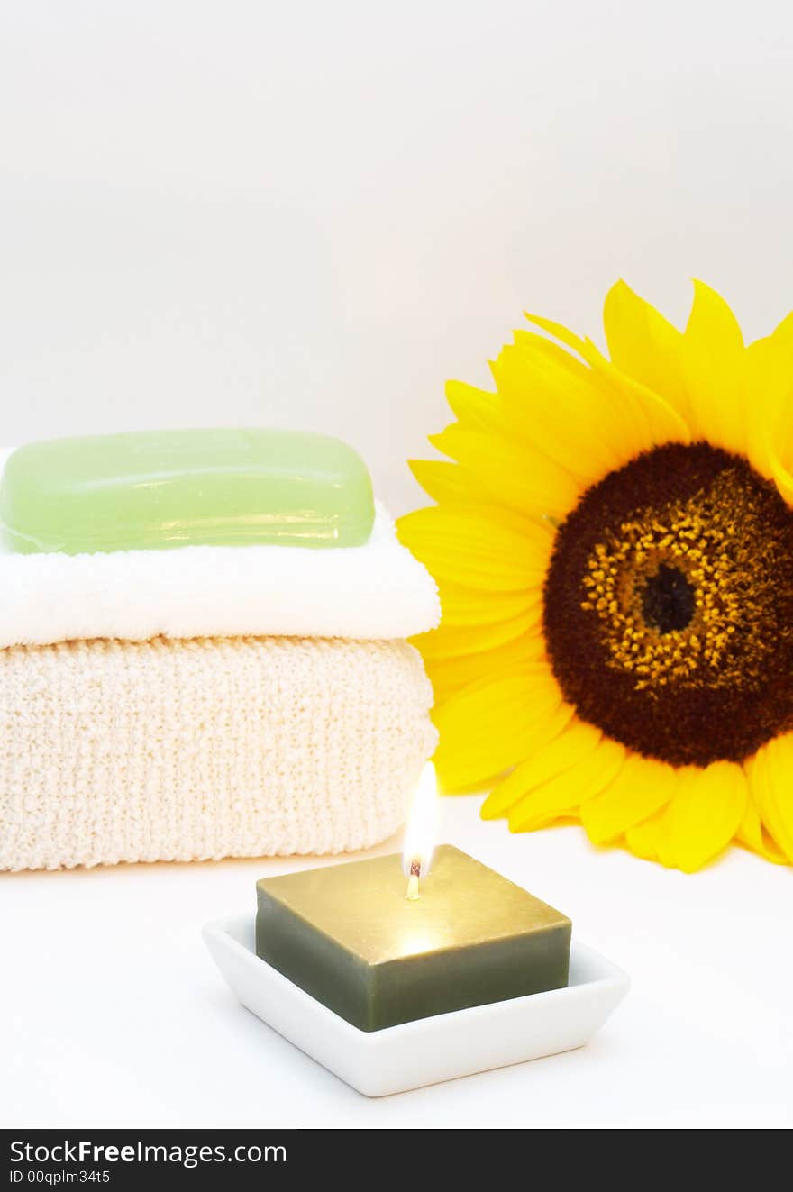 Relaxing spa scene with body sponge, face towel, glycerin soap, candle and sunflower in the background. Relaxing spa scene with body sponge, face towel, glycerin soap, candle and sunflower in the background